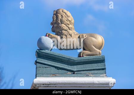 Den Helder, Noord-Holland, Netherlands, April 17, 2021. Side view of a statue of a golden lion with its front legs on a ball, red nails and with its h Stock Photo