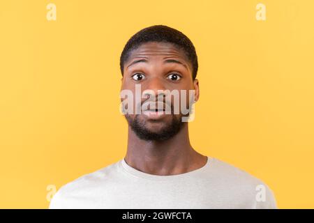 Unbelievable news. Portrait of surprised black guy opening his eyes in shock, looking at camera on yellow background, studio shot, closeup Stock Photo