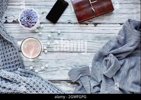 Autumn or winter background shot from top view with hot cocoa, houseplant, cell phone, book, throw blanket and sweater over rustic wood table Stock Photo