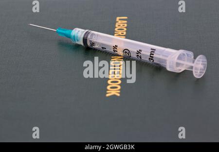 Injection needle placed on scientific Laboratory Notebook reflects that science and medicine are data-based in healthcare, pharmaceuticals, and medica