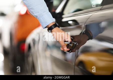 Unrecognizable man open car door, closeup of male hand with watch unlocking black auto door, making test drive at newest automobile showroom. Vehicle, Stock Photo