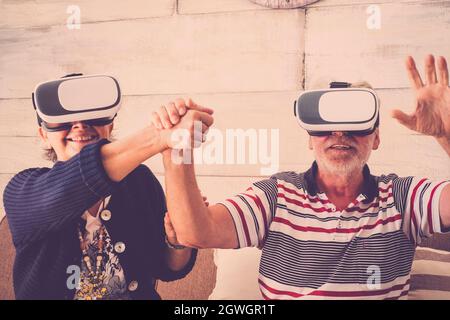 Senior couple having fun using vr headset and operating while holding hands. Elderly couple enjoying virtual reality experience. Old couple enjoying v Stock Photo
