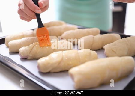 Woman hand is brushing egg yolk onto sweet flour rolls Stock Photo