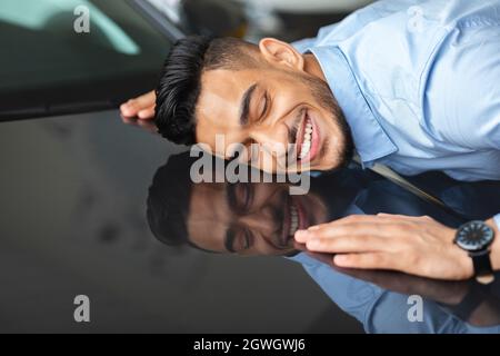 Delighted young arab man hugging car of his dream, closing eyes and smiling, closeup photo, side view, copy space. Happy middle-eastern guy found his Stock Photo