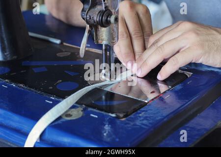 A Closeup shot of male hands sewing white leather on an industrial sewing machine Stock Photo