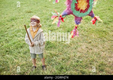 Portrait of boy playing pinata game at Birthday party outdoors and holding bat, copy space Stock Photo