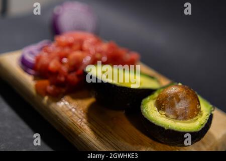 Chopped tomato, sliced onion, and halved avocado on cutting board Stock Photo