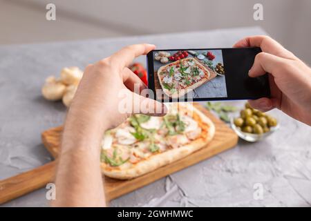 Chef takes pictures of the cooked of italian pizza with parma ham on smartphone. Photographing food and social networks concept. Stock Photo