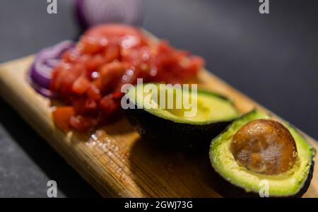 Chopped tomato, sliced onion, and halved avocado on cutting board Stock Photo