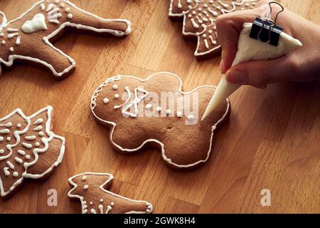 Decorating a homemade gingerbread Christmas cookie in the form of a man with white icing using a cornet Stock Photo