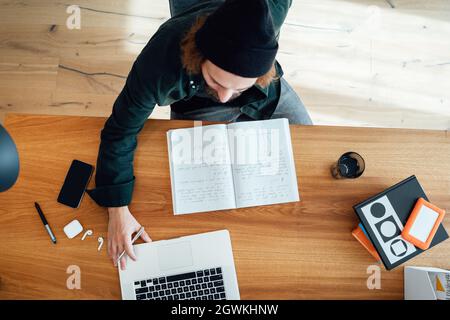 Top view of young university student doing home work while going online education using laptop. Bearded hipster make notes while listening virtual les Stock Photo