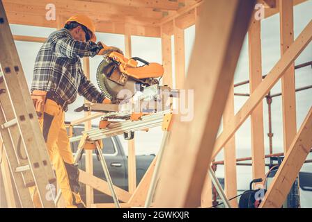 Construction Contractor Worker Using Powerful Wood Saw Inside Wooden Skeleton Frame Of House.