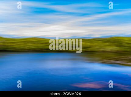 Abstract background created by camera motion of a river bank with the blue sky reflecting in the water. Stock Photo
