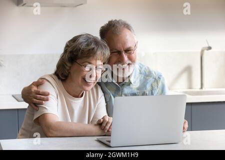 Happy bonding mature couple using computer at home. Stock Photo