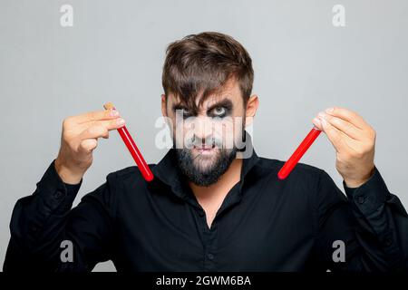 a bearded man with undead makeup for Halloween holds test tubes in which red liquid Stock Photo