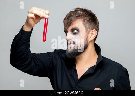 a bearded man with undead makeup for Halloween holds test tubes in which red liquid Stock Photo