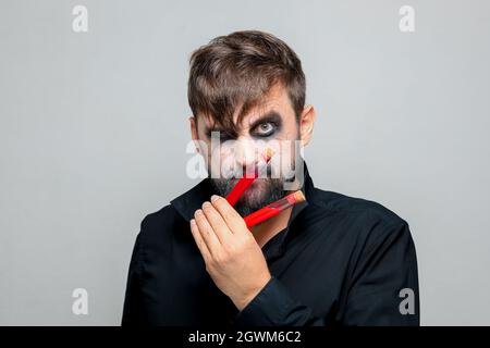 a bearded man with undead makeup for Halloween holds test tubes in which red liquid Stock Photo