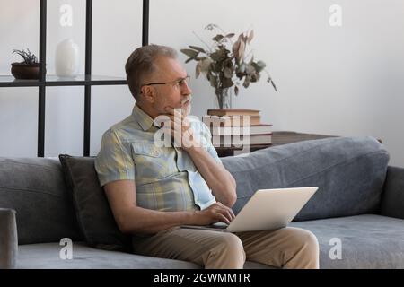 Pensive middle aged 60s man using computer. Stock Photo