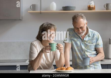 Happy middle aged mature family couple eating breakfast in kitchen. Stock Photo