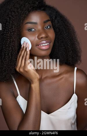 Beautiful happy black girl purifying skin with cotton pad. Skincare concept. Stock Photo