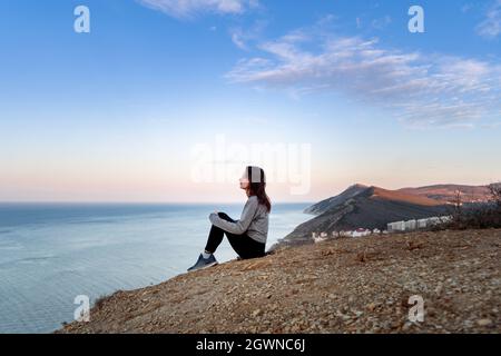 Middle age sporty woman feel harmony and enjoy the beautiful view in the mountains. She sitting on rocks and looking on sea. Soul searching, digitak d Stock Photo