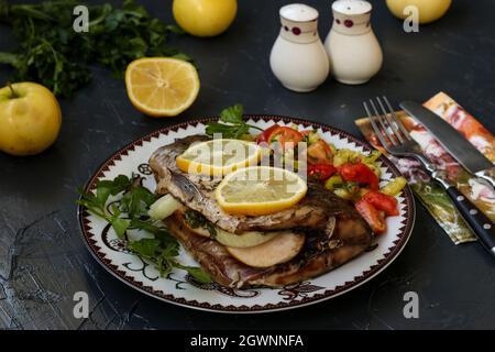 Baked fish on a plate with lemon, salad and greens. Stock Photo