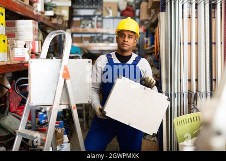 Portrait of worker in protective helmet and overalls with toolbox in hardware store Stock Photo