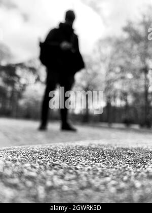 A grayscale shot of the silhouette of a person standing on the road in the blurry background Stock Photo