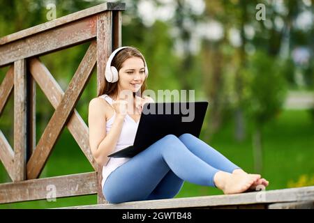 Woman in cordless headphones works with laptop outside. Stock Photo