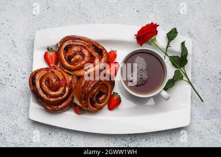 Plate with tasty strawberry buns, cup of tea and rose on light background Stock Photo