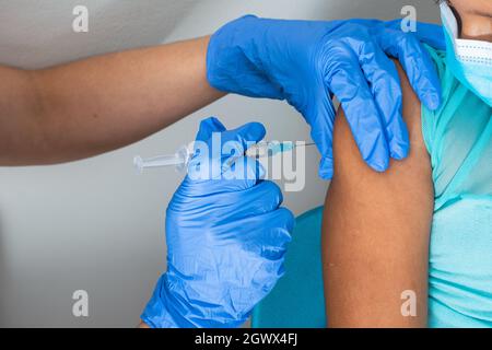 children's nurse injecting arm of little brown girl, girl watching injection. doctor's hands with rubber gloves injecting covid-19 or flu vaccine. med Stock Photo