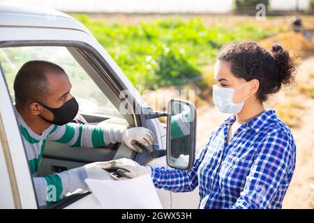 Farmer couple in protective masks discussing papers near car Stock Photo