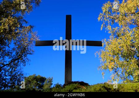 Metallic cross against blue sky, with autumnal trees in the background. Stock Photo