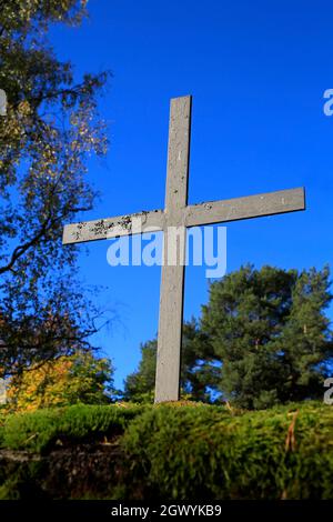 Old metallic cross against blue sky, with autumnal trees in the background. Stock Photo
