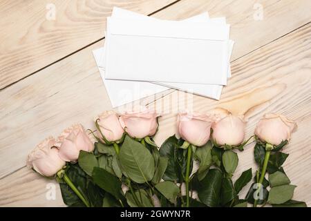 Bunch of beautiful pink roses on wooden table. White envelopes with letters in them. Pleasant surprise. Romantic gift for holiday. Stock Photo