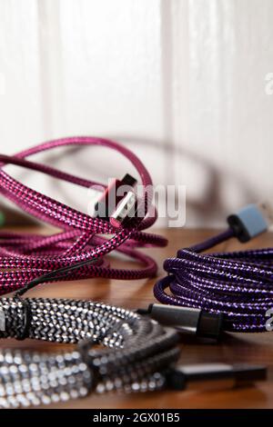 Pink charging cord next to purple and silver charging cords on a wooden table Stock Photo
