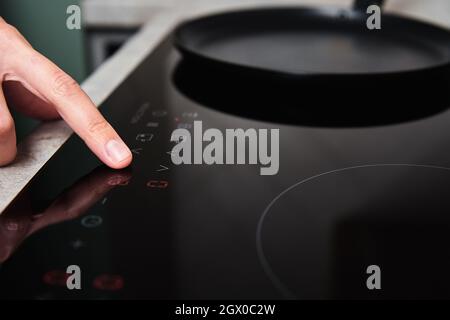Modern kitchen appliance. Woman hand turn on induction stove to cook. Finger touching sensor button on induction or electrical hob Stock Photo