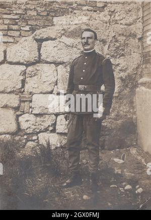 middle aged man posing for the camera in front of a castle at unknown place. This man is police officer or military officer but unrecogniseable that which empire's officer him. He has got black uniform, pistol holster, and a big massive impressive belt buckle. He hes got quite fashonable moustache. Period late 19th century early 20th century. Source: original photograph Stock Photo