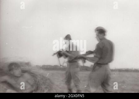 vintage / Retro army / military PPsh-41 series 2. Two soldiers are caught a person who possibly wanted to escape to the free world ( outside of the iron curtain) holding against him them  Soviet submachine gun ( papasha design by Georgy Shpagin ) on the field  around at the 1950's. They are from Eastern Europe possibly Hungary. he PPSh-41 was in service from 1941-1960's. Source: original photograph. Stock Photo