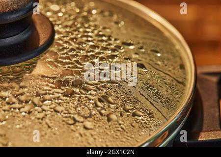Drops on the glass lid of frying pan preparing dish on the oven with selective focus Stock Photo