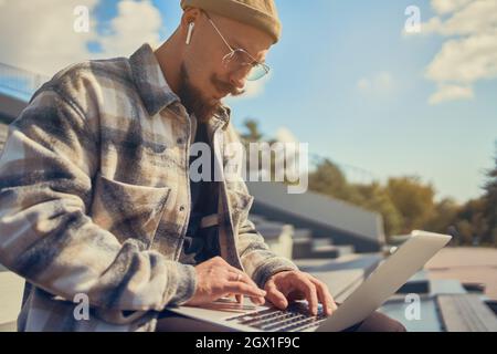 Handsome bearded student man in glasses studies while sits near the university types on the laptop Stock Photo