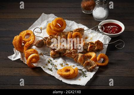 From above of tasty deep fried potato curls and skewers with pork meat pieces against tomato sauce and condiments on brown background Stock Photo