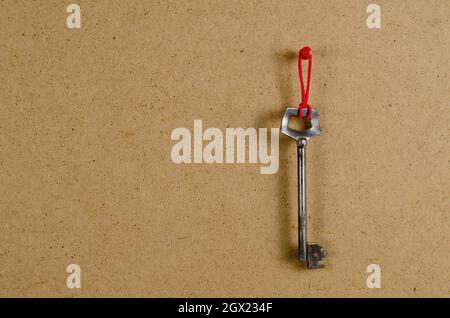 A large metal door key opposite the brown background. The old key hangs vertically on a red rubber band. Side view. Copy space Stock Photo