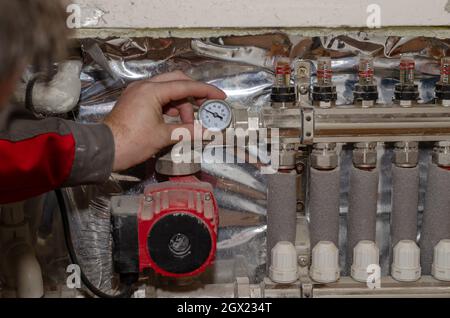 Professional service of heating systems concept. Specialist makes adjustments to the floor heating system. An adult male checks the temperature on the Stock Photo