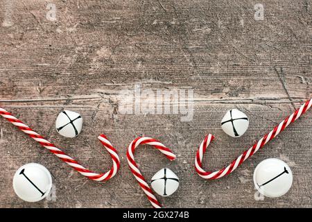 Candy canes and jingle bells on brown weathered wood. Christmas background. Stock Photo