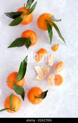 Top view of whole clementines with leaves, peel and segments on gray patterned background. Stock Photo