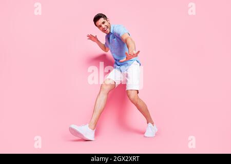 Photo of funky positive guy walk having fun wear blue shirt shorts sneakers isolated on pink color background Stock Photo