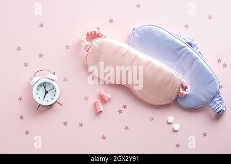 Flat lay sleeping mask, alarm clock, earplugs and pills on pink background. Insomnia treatment concept. Stock Photo