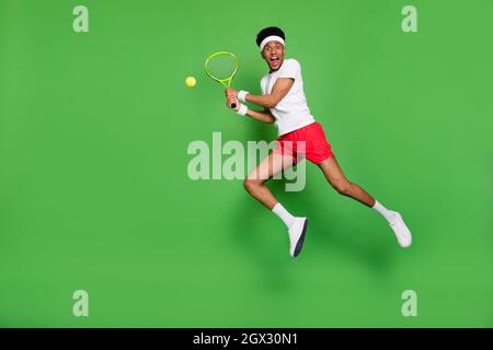 Full length photo of cute funky dark skin man wear white t-shirt jumping high playing squash isolated green color background Stock Photo