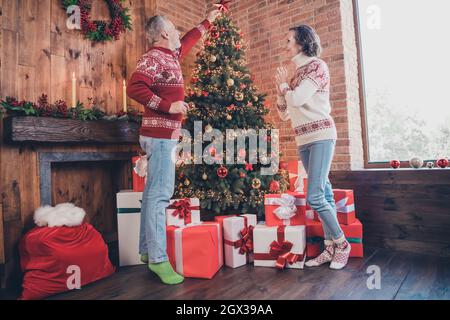 Full length body size photo senior wife and husband decorating evergreen xmas tree Stock Photo